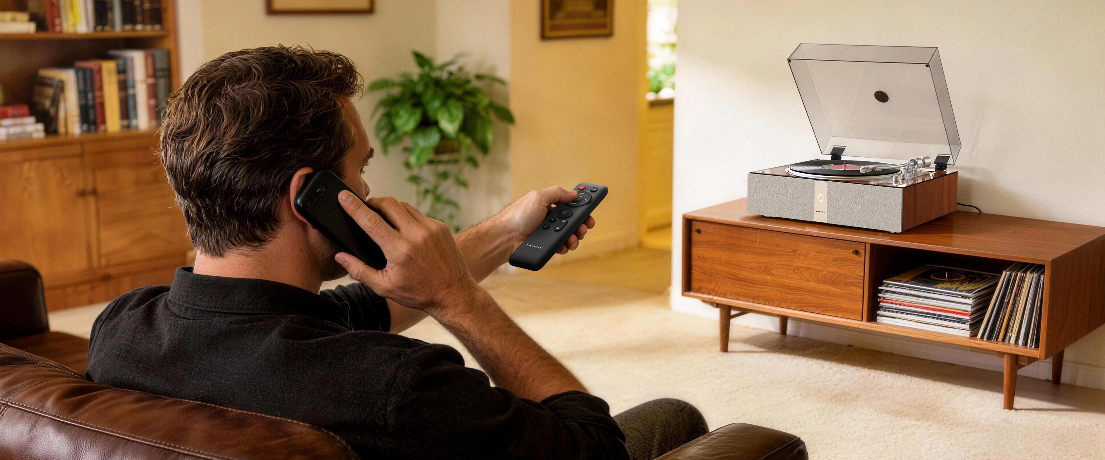 Man using a remote to control a automatic record player from the sofa.