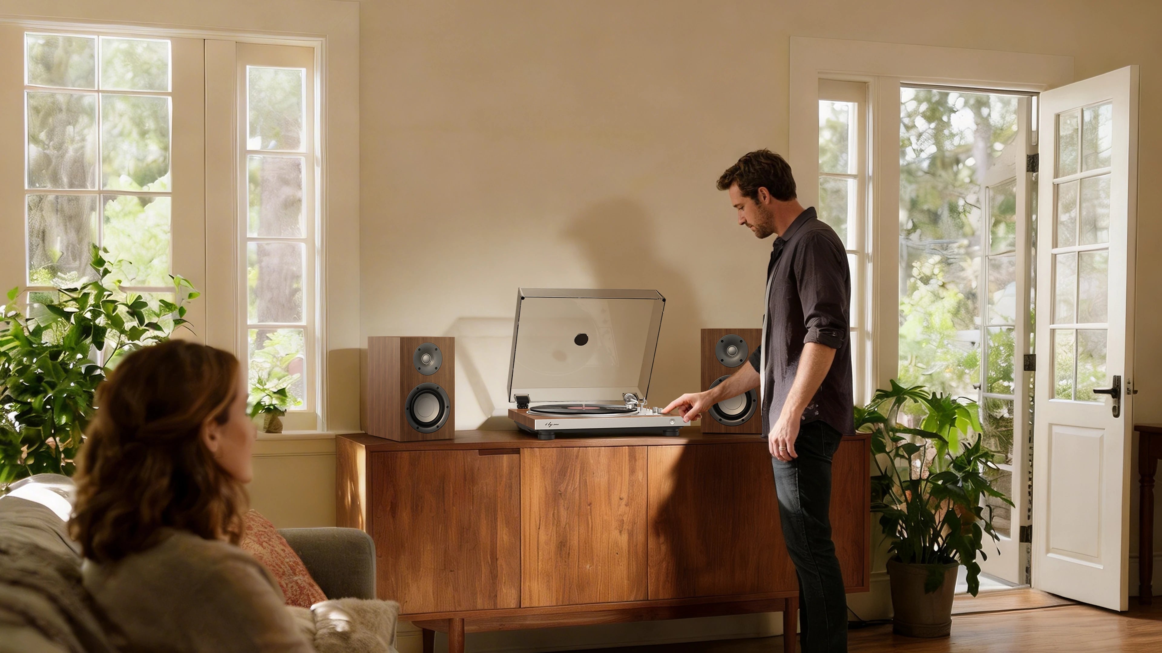 Man starts a fully automatic record player in a sunlit living room, featuring a built in preamp and phono cartridge.