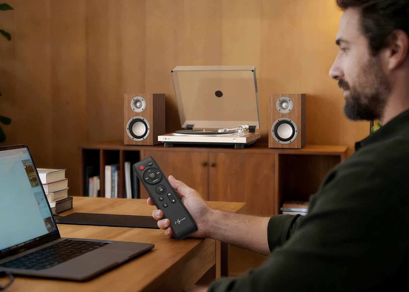 Man uses remote for automatic record player at desk, enjoying convenience with this all in one turntable set.