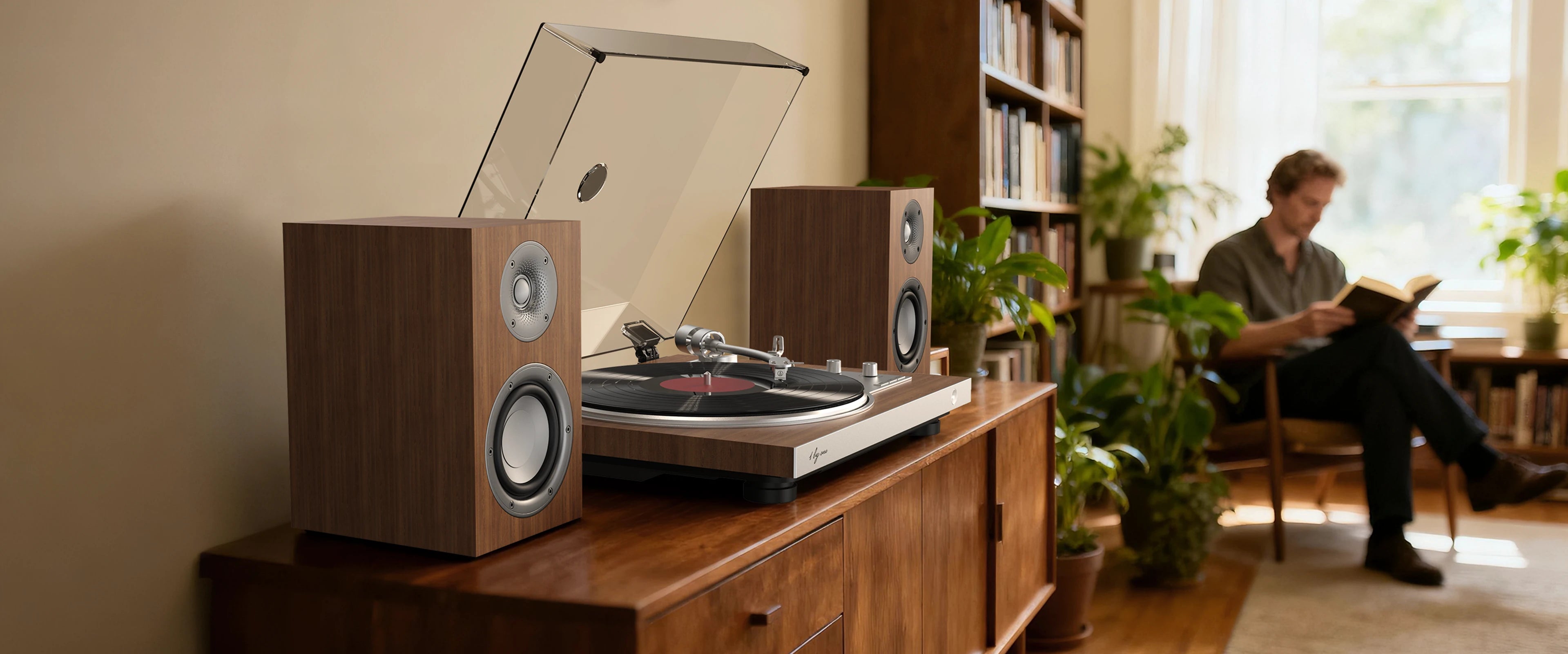 Man reads by vintage record player, featuring a fully automatic turntable and bookshelf speakers on sideboard in a study.