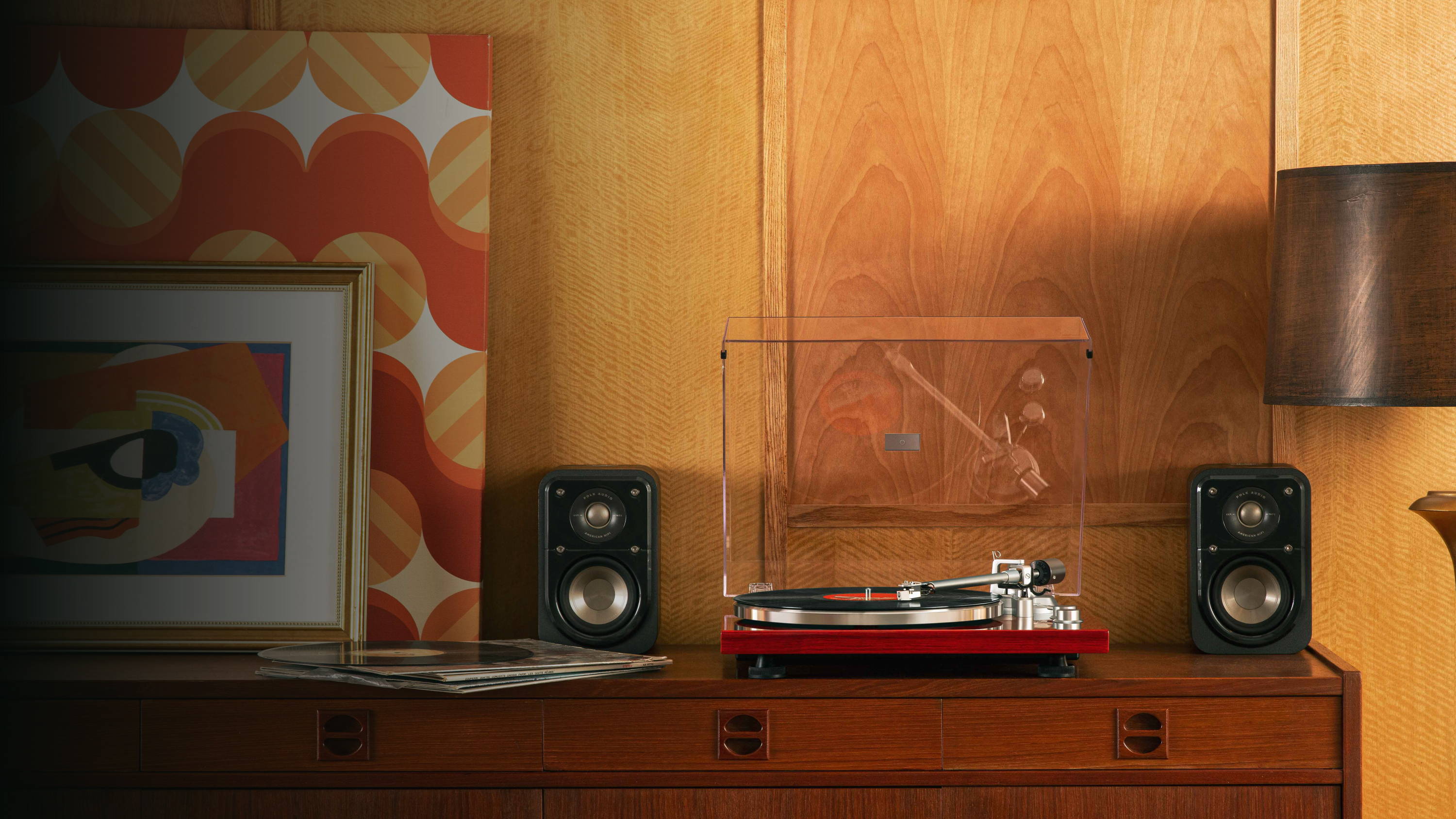 Mahogany turntable with speakers on a wood console in a retro living room with vinyl and framed art