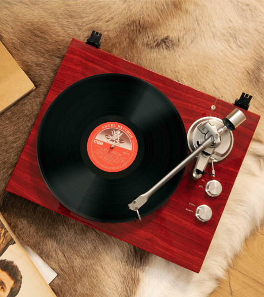 Woman relaxing with vinyl beside a top-down mahogany bluetooth turntable for old records on a fur rug