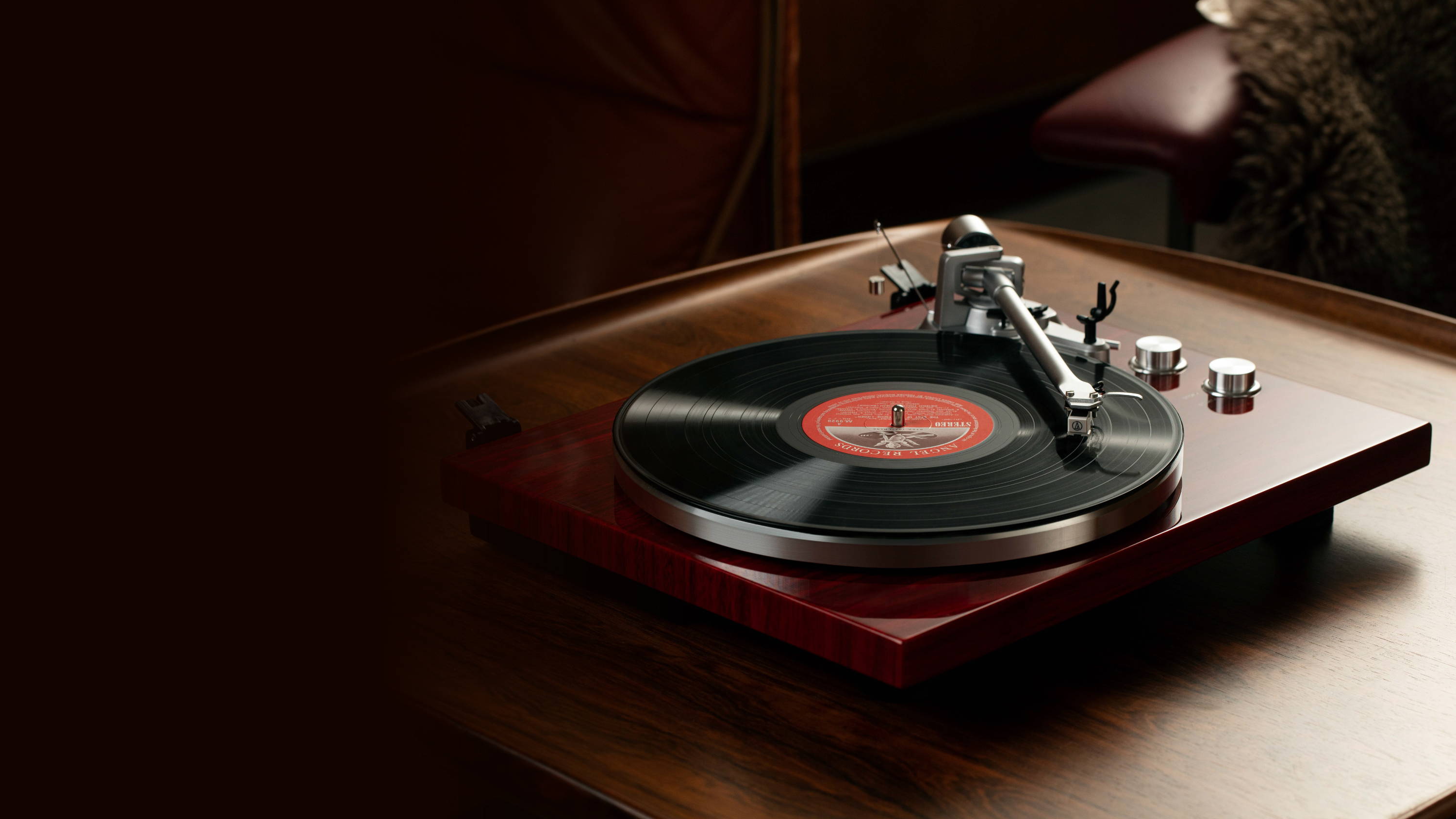Mahogany retro record turntable playing a vinyl LP, with tonearm and silver control knobs