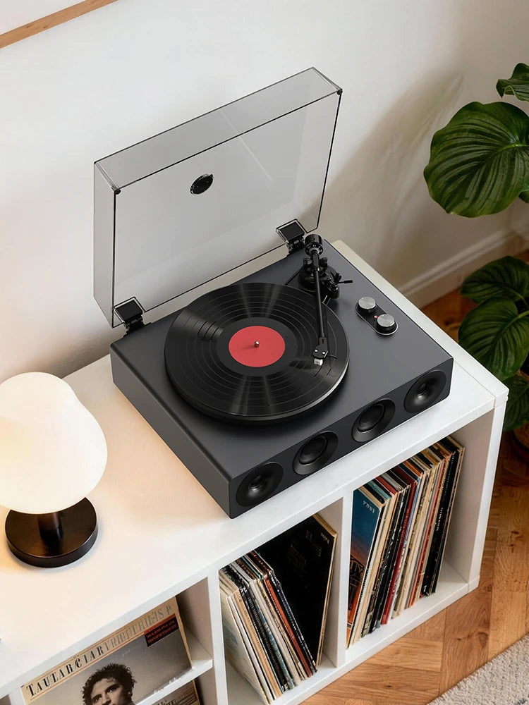 Grey all-in-one record player with built-in speakers playing a vinyl LP, dust cover open, on a white vinyl stand