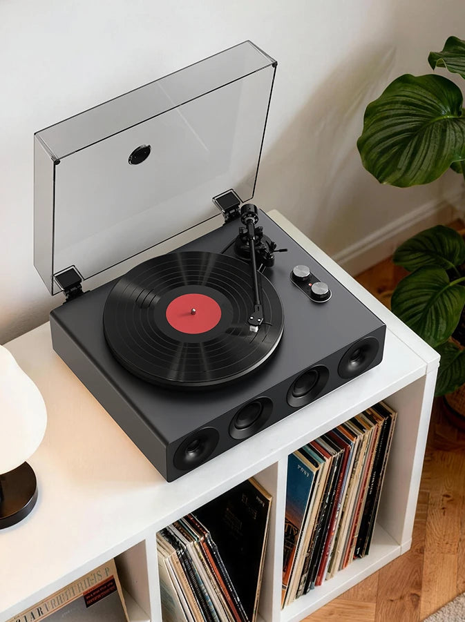 Grey all-in-one record player with built-in speakers playing a vinyl LP, dust cover open, on a white vinyl stand