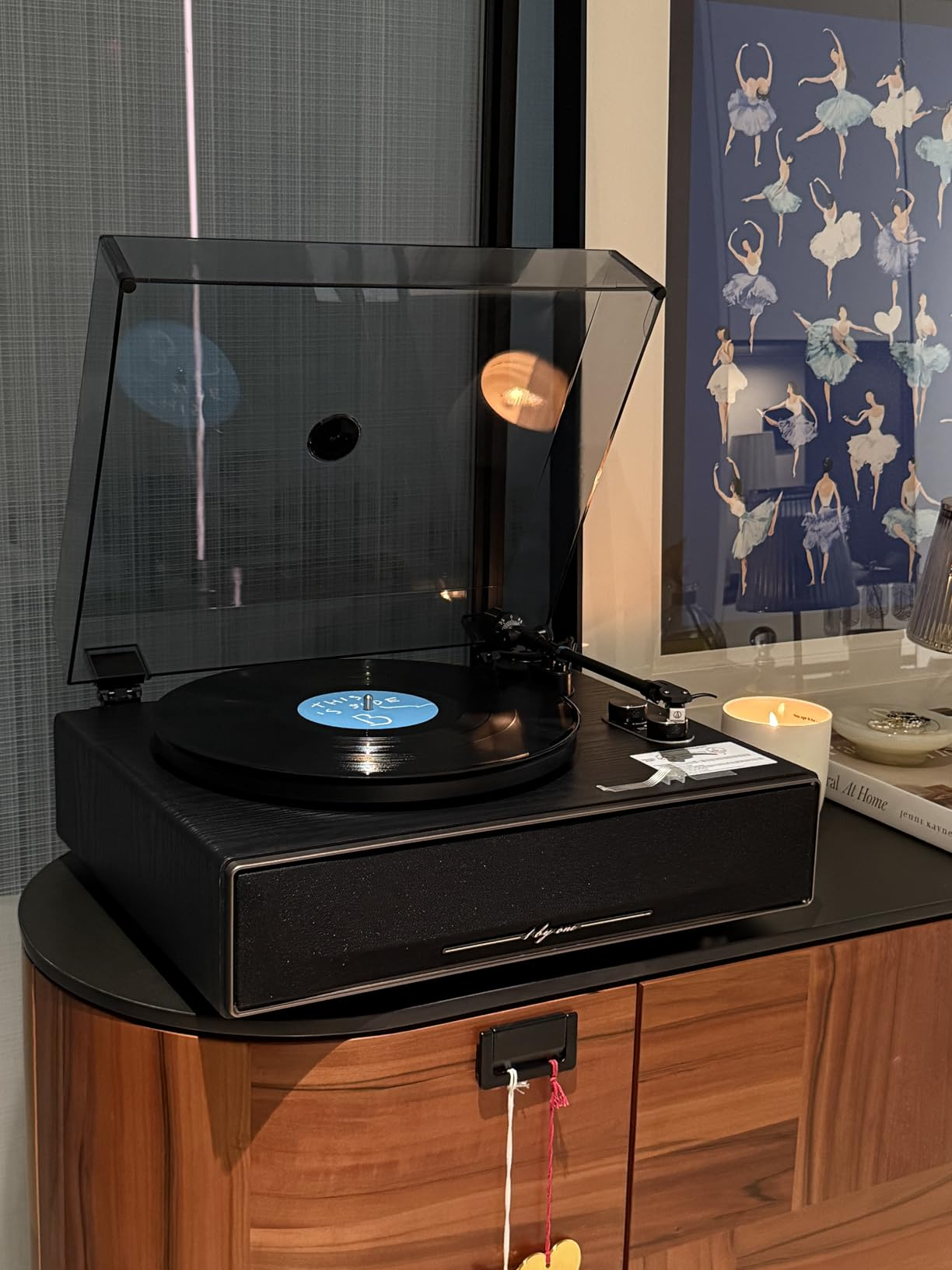 A stylish black Bluetooth record player sits on a mid-century modern sideboard next to a scented candle.
