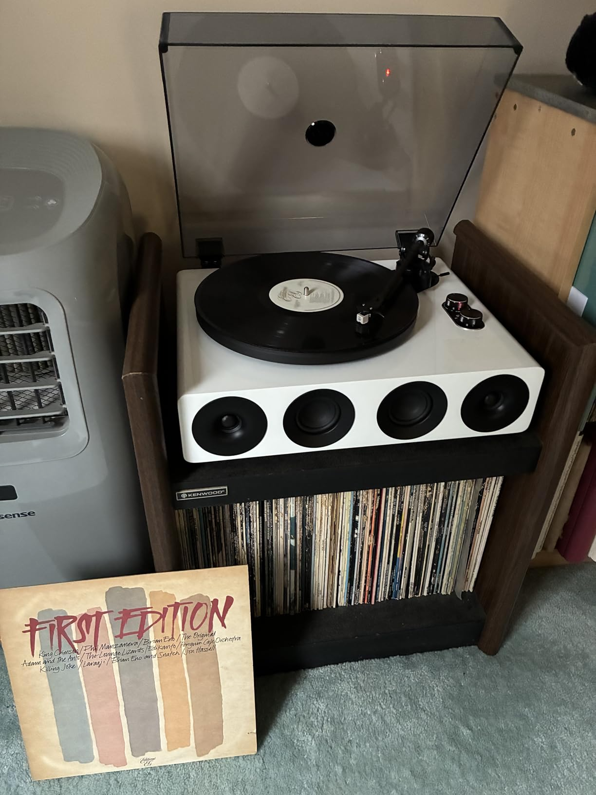 A modern white record player with built-in speakers sits on a storage rack.